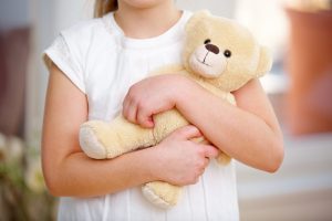 Hände von Kind halten Teddybär als Kuscheltier im Arm